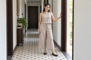 Woman wearing taupe cropped wide-leg trousers, a matching sleeveless blouse, and black Tabi flats in a tiled hallway.