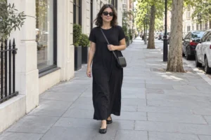 Woman wearing a relaxed black maxi dress, black crossbody bag, sunglasses, and black Tabi flats on a city sidewalk.
